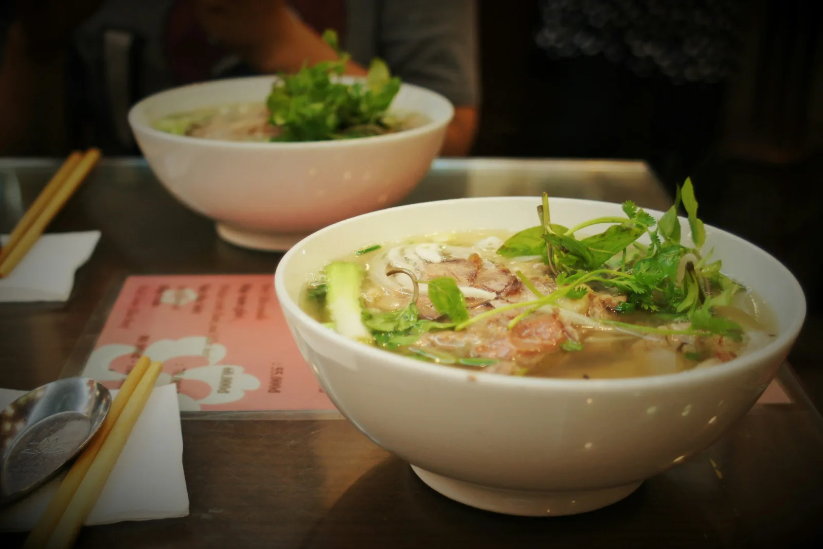 Hai bát phở bò nóng, rắc hành và rau thơm, trên bàn ăn sáng